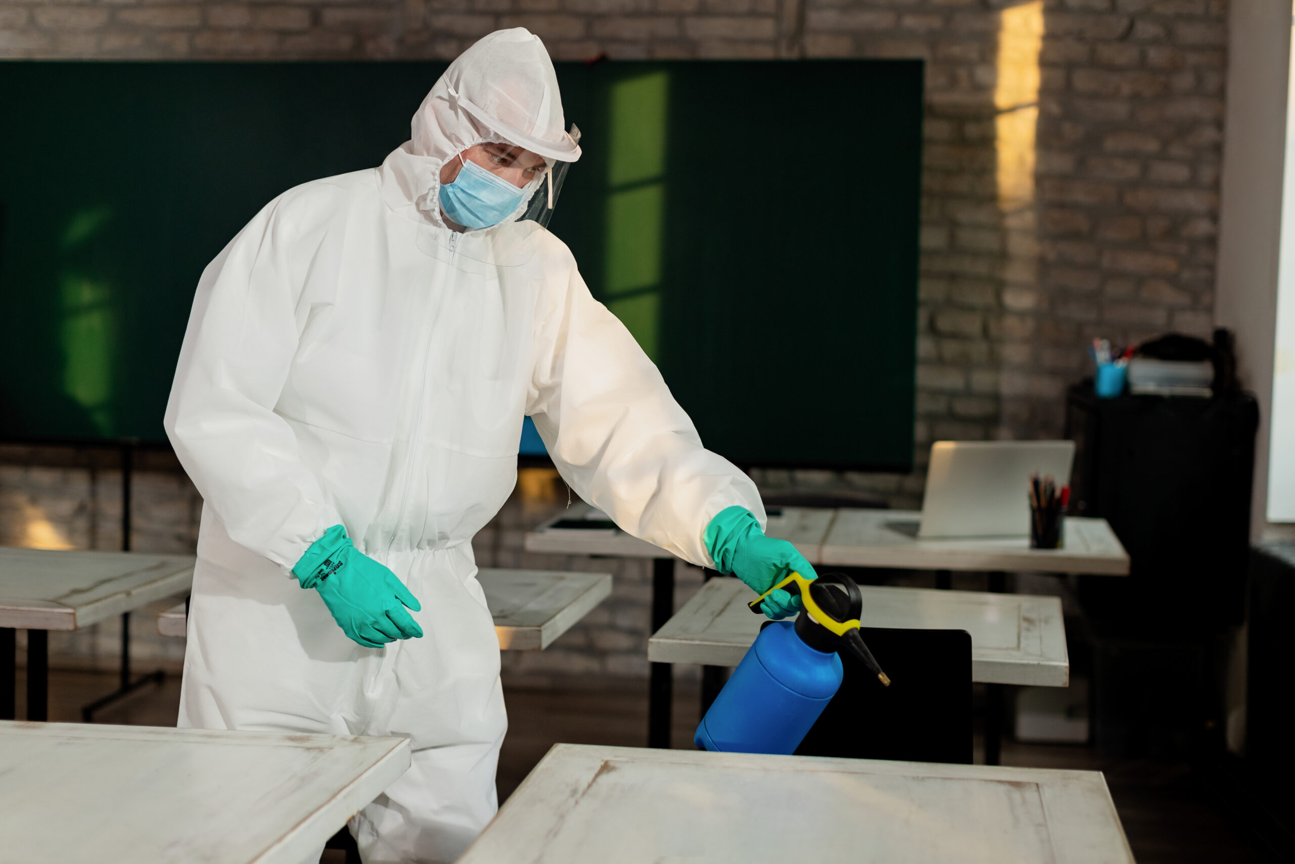Services man in hazmat suit disinfecting classroom due to coronavirus pan