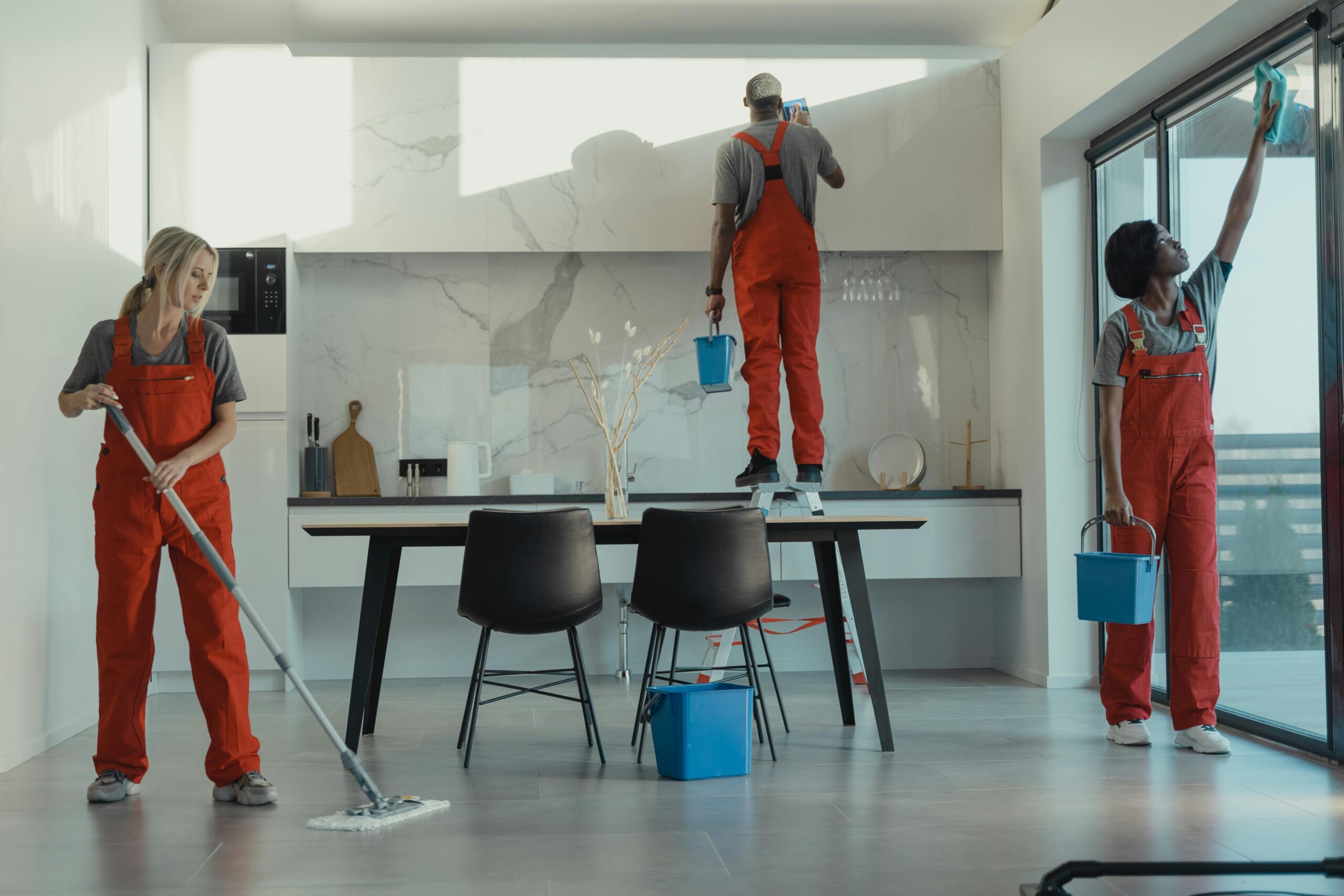 Services Group of cleaners in red uniforms mopping and wiping glass in a modern dining room.