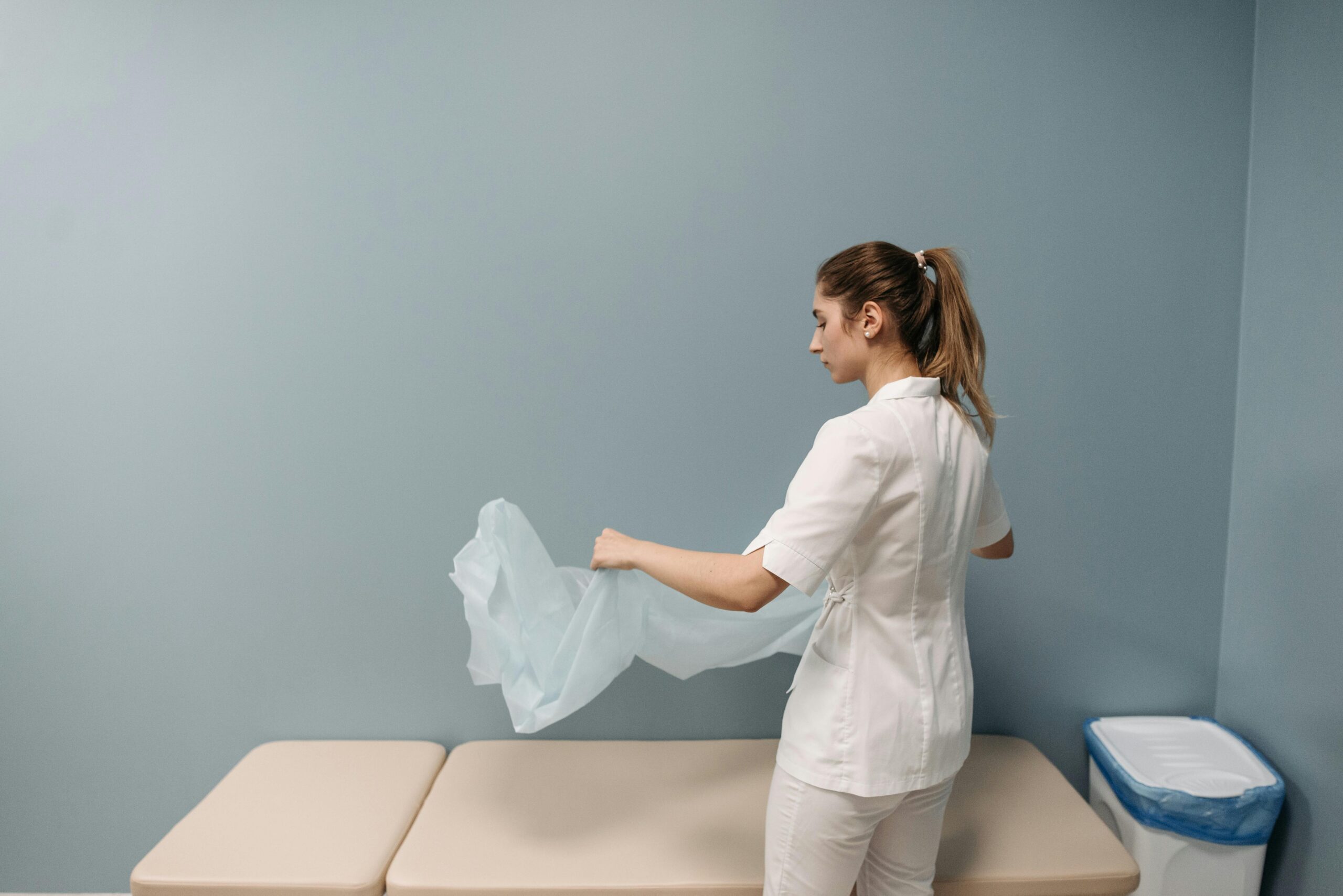 Services A nurse prepares an examination table in a healthcare facility, ensuring cleanliness and safety.
