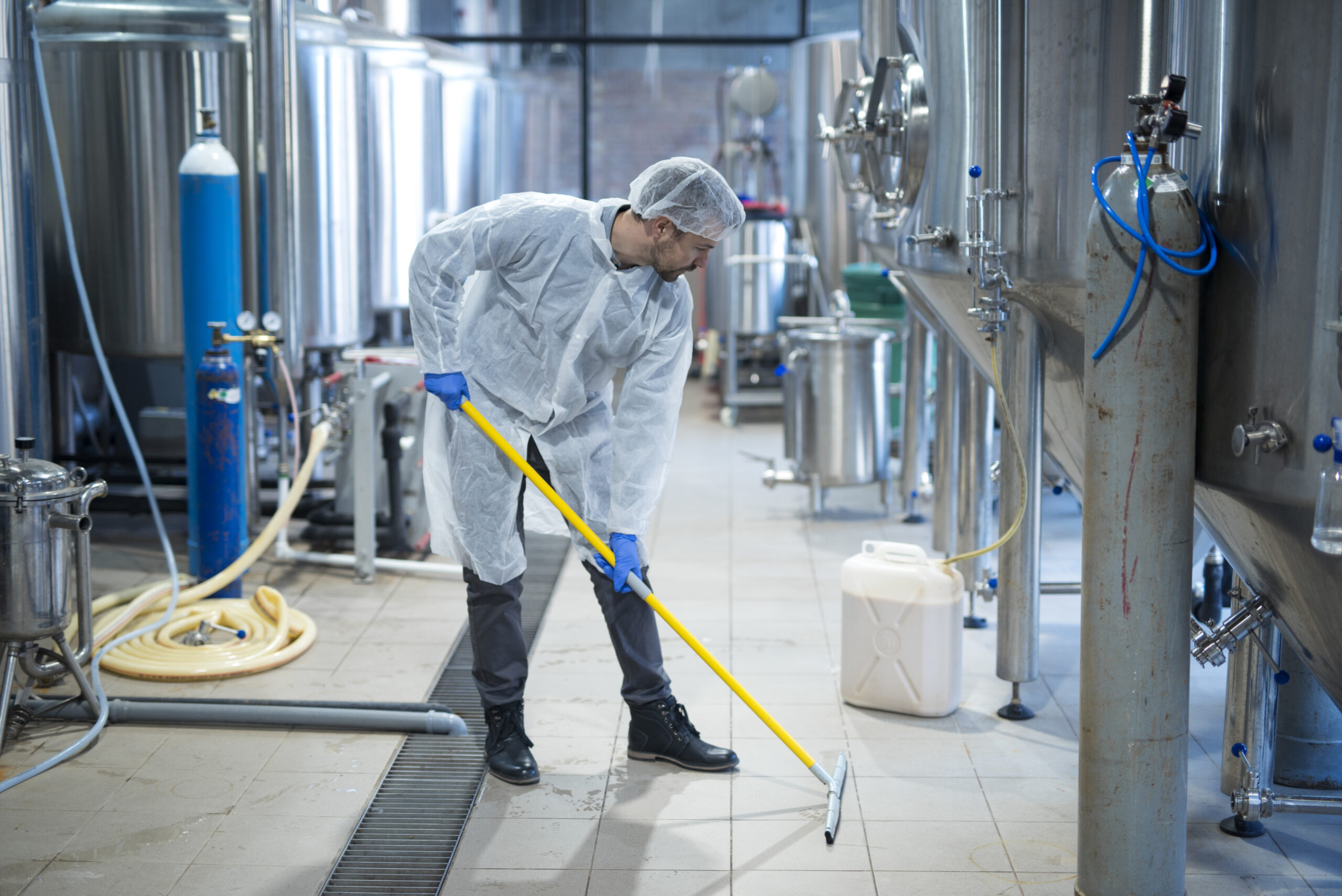 Services professional industrial cleaner in protective uniform cleaning floor of food processing plant.